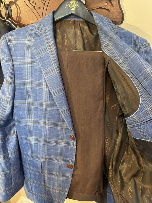 Light blue plaid sport coat with brown buttons over brown trousers, bronze lining printed with shoe sketches