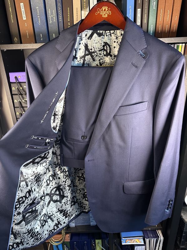 Navy two-button suit on a hanger, opened to show a pale blue lining printed with black graffiti lettering